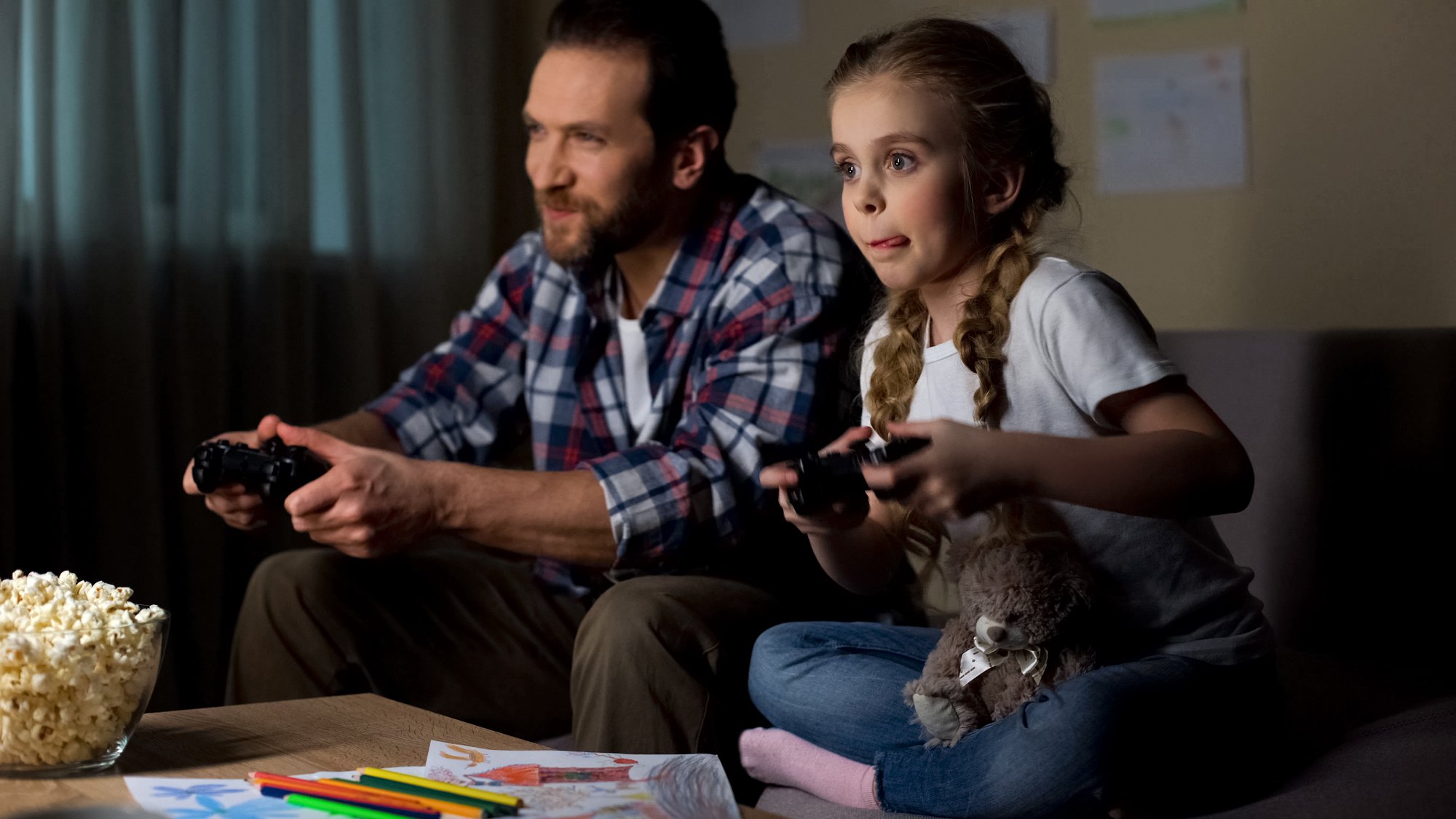 Dad and little child playing video game with joysticks together home, having fun