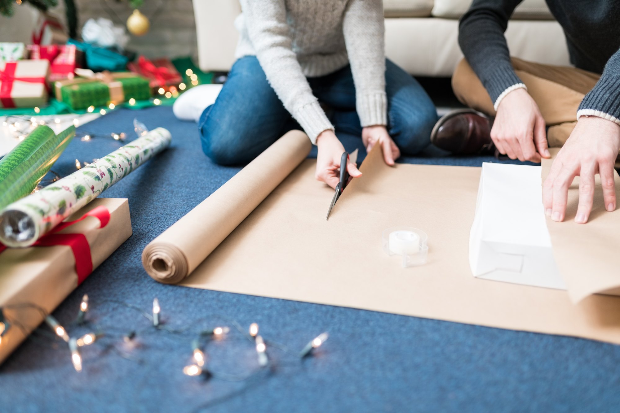 Low section of woman cutting paper while assisting partner in wrapping present at home during Christmas