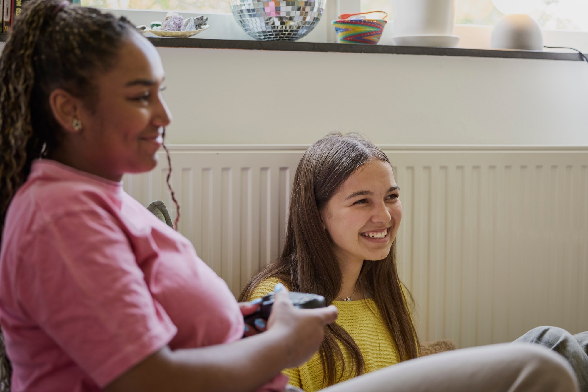 Smiling female teenager playing video game by friend at home