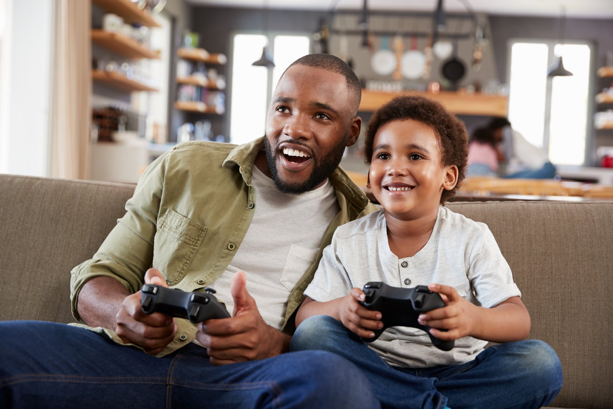 Father And Son Sitting On Sofa In Lounge Playing Video Game