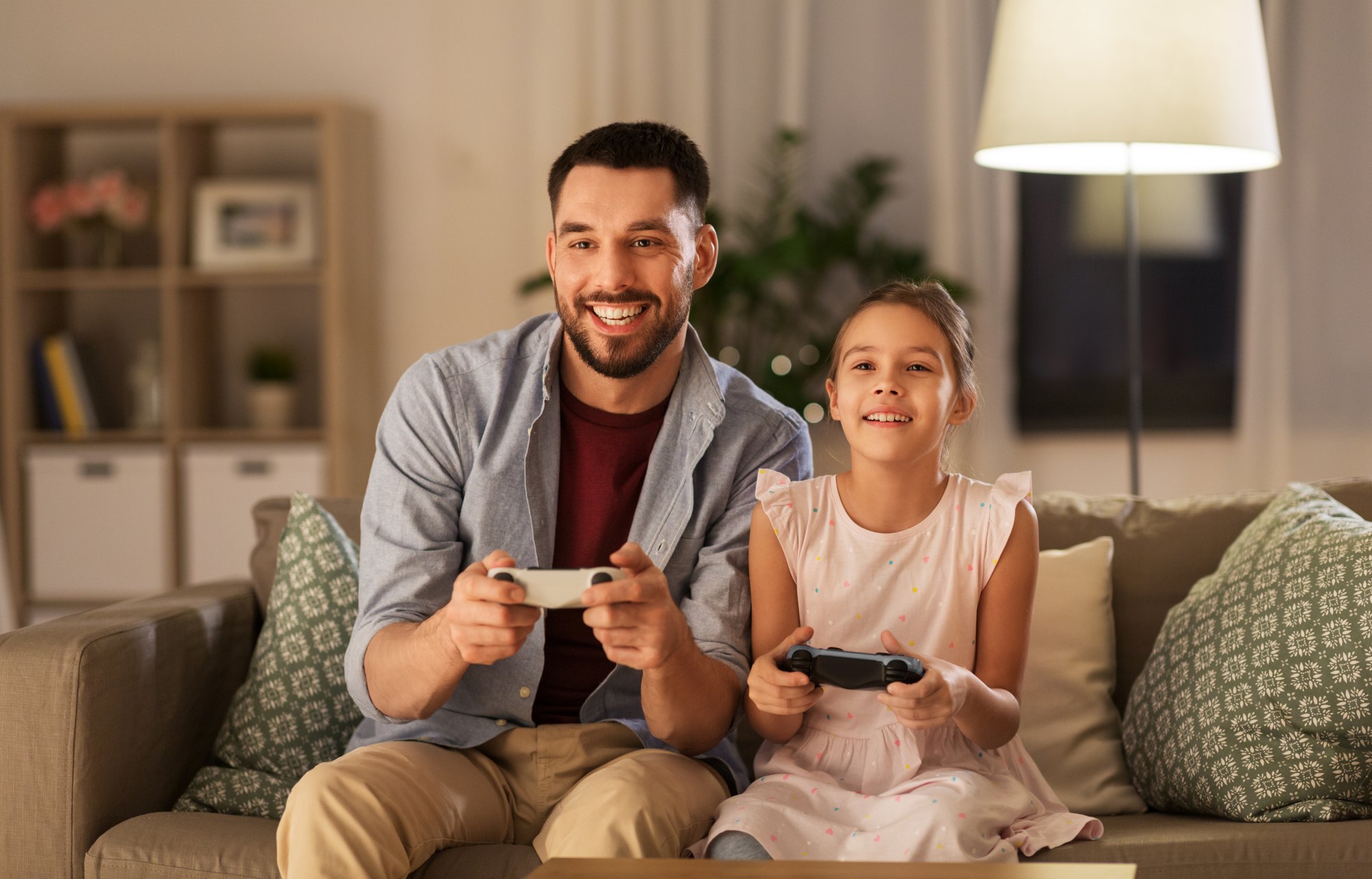 Happy father and little daughter with gamepads playing video game at home