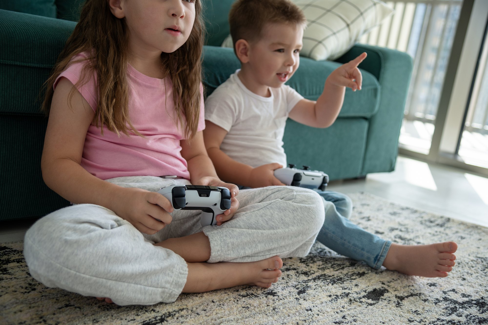 Children with joysticks playing video games on the floor at home